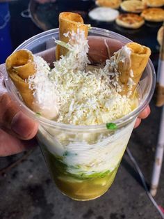 a person holding up a plastic cup filled with food and cheese on top of it