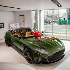 a green sports car with a red bow on it's hood in a showroom