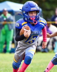 a young boy running with a football in his hand while wearing a blue and yellow uniform