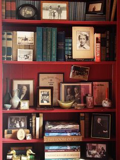 a bookshelf filled with lots of books and pictures on top of red shelves