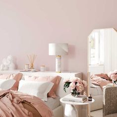 a bedroom with pink walls, white furniture and flowers in vases on the table