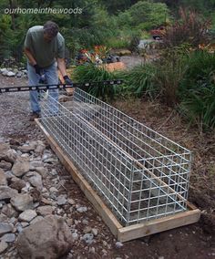 a man is working in the garden with a metal fence and rock pile next to it