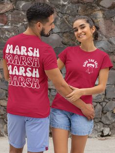 a man and woman standing next to each other in front of a stone wall wearing matching shirts