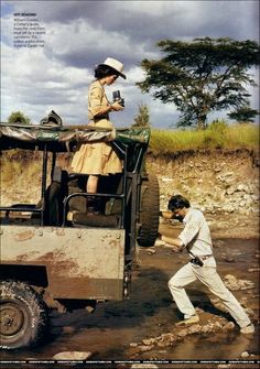 a man and woman standing on top of a truck in the mud near a river