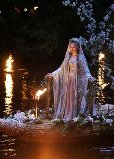 a woman dressed in white standing next to a statue with candles and flowers on it