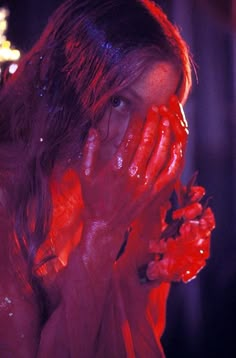 a woman covered in red paint holding her hands to her face and looking at the camera