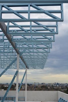 a metal structure on top of a building with blue railings and benches underneath it