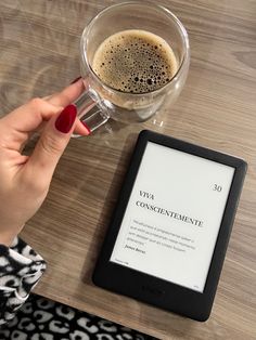 a woman's hand holding a tablet next to a cup of coffee