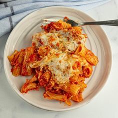 a white plate topped with pasta covered in sauce and cheese next to a blue towel