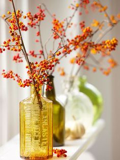 two yellow vases with red berries in them on a white shelf next to each other