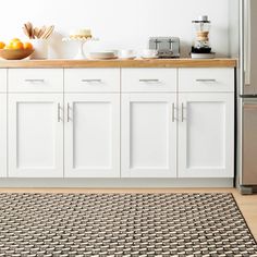 a kitchen with white cabinets and an area rug in front of the counter top that has oranges on it