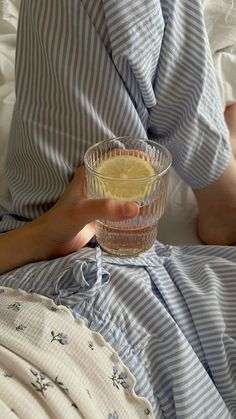 a person laying in bed holding a glass cup with lemonade on top of it