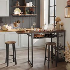 a kitchen with two stools and a table in front of the window, filled with dishes