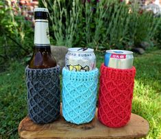 three crocheted can coolers sitting on top of a wooden stump in the grass