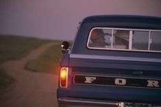 the back end of a blue pickup truck driving down a country road at night time