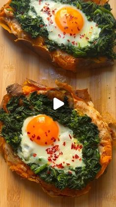 two pieces of bread with eggs and spinach on them, sitting on a wooden surface