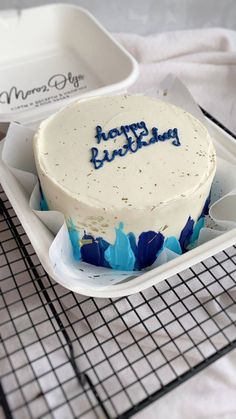 a birthday cake with blue frosting sitting on a cooling rack next to a baking tray