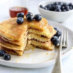 a stack of pancakes with blueberries and syrup on a plate next to a fork