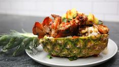 a pineapple with meat and vegetables in it on a white plate next to a green plant