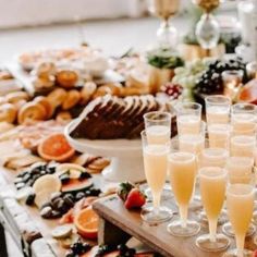 champagne flutes are lined up on a tray with fruit and pastries in the background