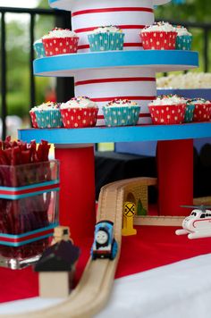 there is a train and cupcakes that are on the cake stand at this birthday party