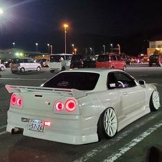 a white car parked in a parking lot at night with its lights on and the tail lights turned red