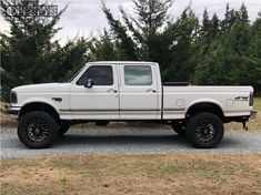 a white pick up truck parked on top of a gravel road in front of trees