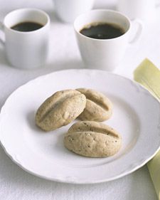 three cookies on a white plate next to two cups of coffee and a yellow napkin