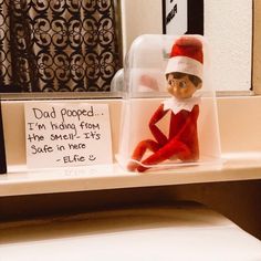 an elf is sitting on top of a shelf in front of a sign that says, dad pooped i'm hiding from the smell