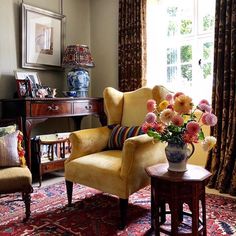 a yellow chair sitting in front of a window next to a table with flowers on it