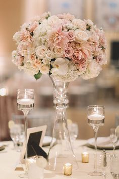 a vase filled with pink and white flowers on top of a table next to candles