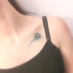 a woman's chest with a peacock feather tattoo on the left side of her shoulder