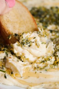 a person dipping something into a white bowl filled with cream cheese and spinach leaves