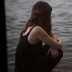 a woman sitting on the edge of a body of water with her back to the camera