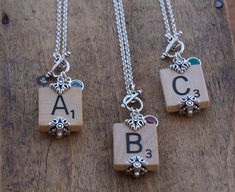 three necklaces with letters and charms hanging from them on a wooden surface, one has a charm that says abc