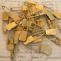 lots of gold colored clothes pins on top of a piece of paper with writing in the background