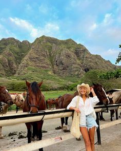 a woman standing in front of horses with mountains in the backgrouds behind her