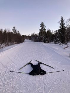 a person laying on the ground with their skis in the snow near some trees