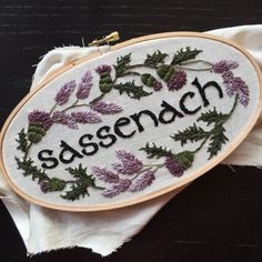 an embroidered sign with the word sassenach on it and some flowers around it