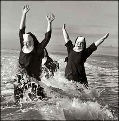 black and white photograph of two women in the ocean with their arms up, both wearing nun costumes