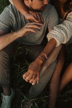 two people sitting in the grass with their hands on each other's chests