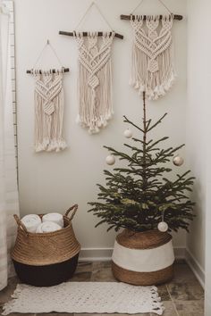 a small christmas tree in a basket next to two wall hangings with balls and tassels on them