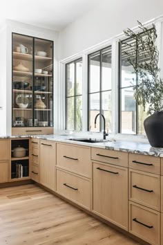 a kitchen with wooden cabinets and white counter tops, black vases on the window sill