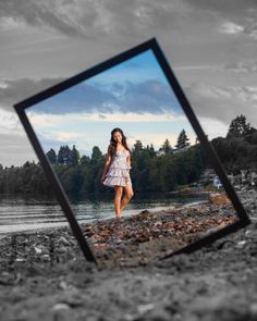 a woman in a white dress is standing on the beach and looking at her reflection