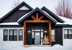 a black and white house with a christmas tree on the front porch in the snow