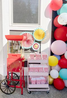 an outdoor party with balloons, popcorn buckets and a cart in front of the door