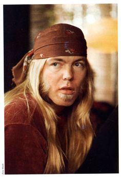 a man with long blonde hair wearing a bandana and looking at the camera while sitting down