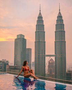 a woman sitting on the edge of a swimming pool in front of two tall buildings