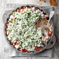 a dish filled with vegetables and cheese on top of a white cloth next to chips