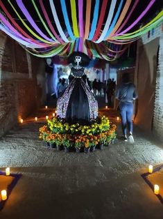 a colorful display in the middle of a walkway with candles lit up around it and a skeleton wearing a hat on top